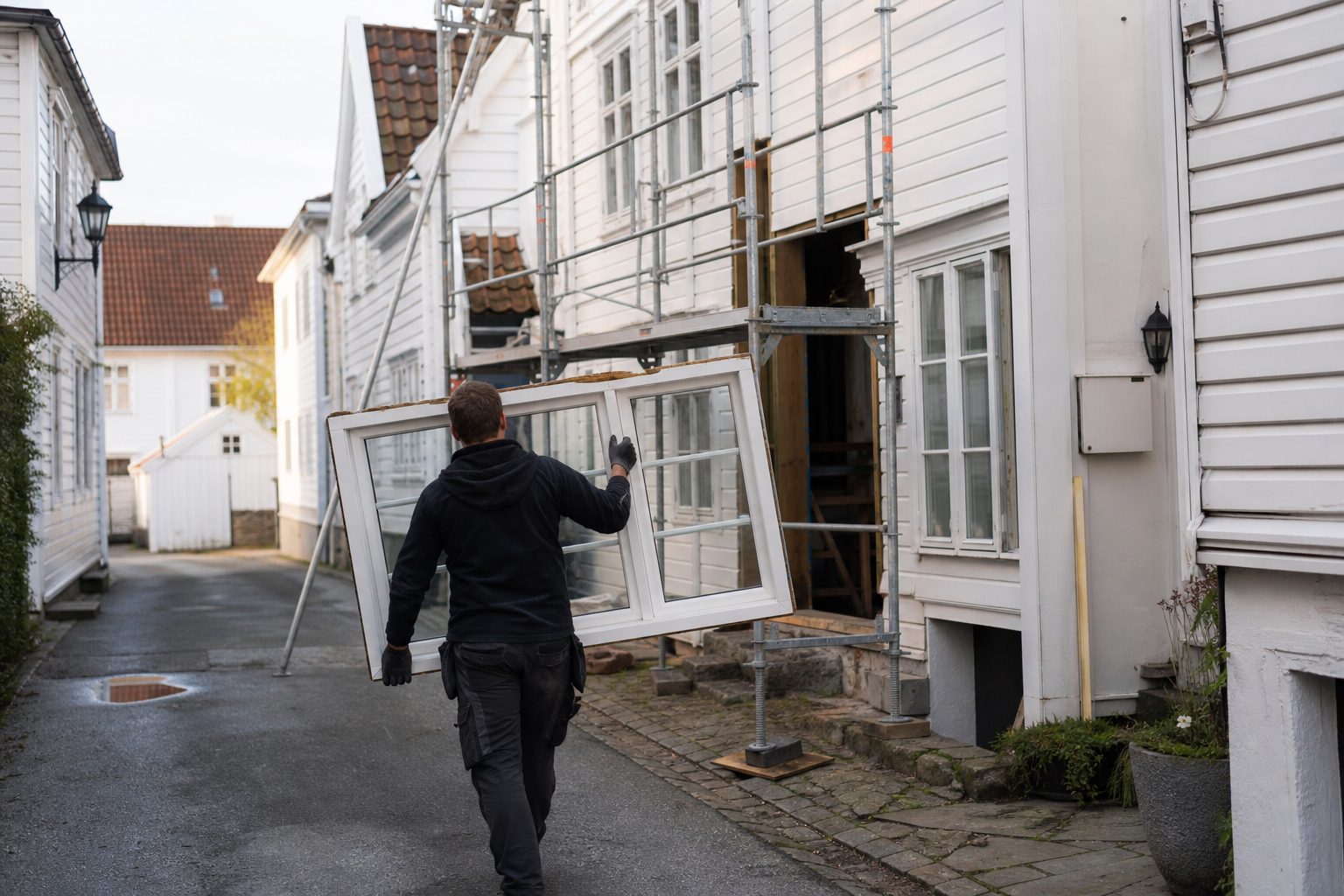 Et gammelt, hvitmalt trehus i en smal gate i Stavanger sentrum, med stillas langs fasaden.