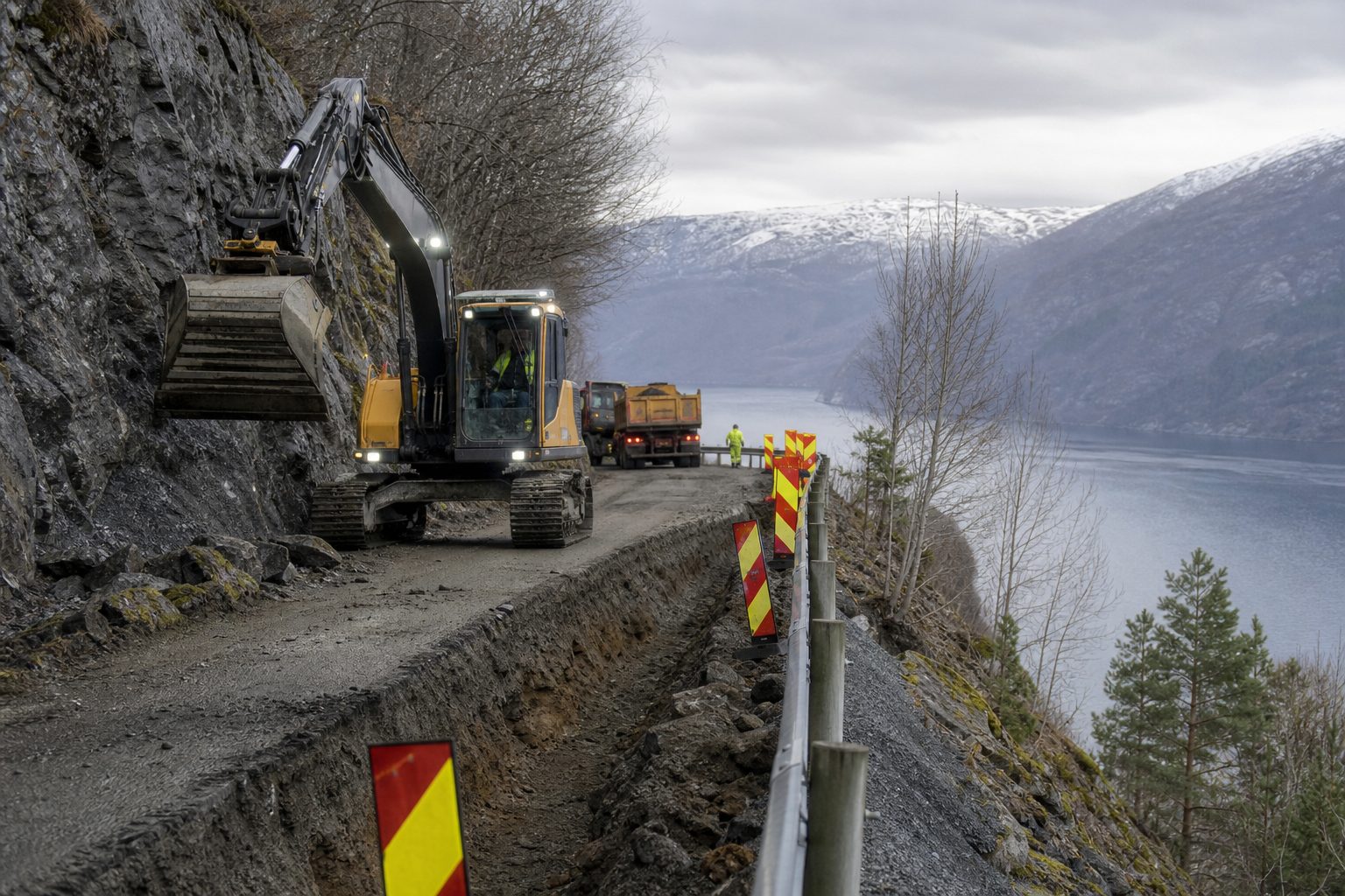 En smal fylkesvei langs en fjellside i Sogn med anleggsmaskiner, nyopprettet grøft og avsperringer i grått høstlys.