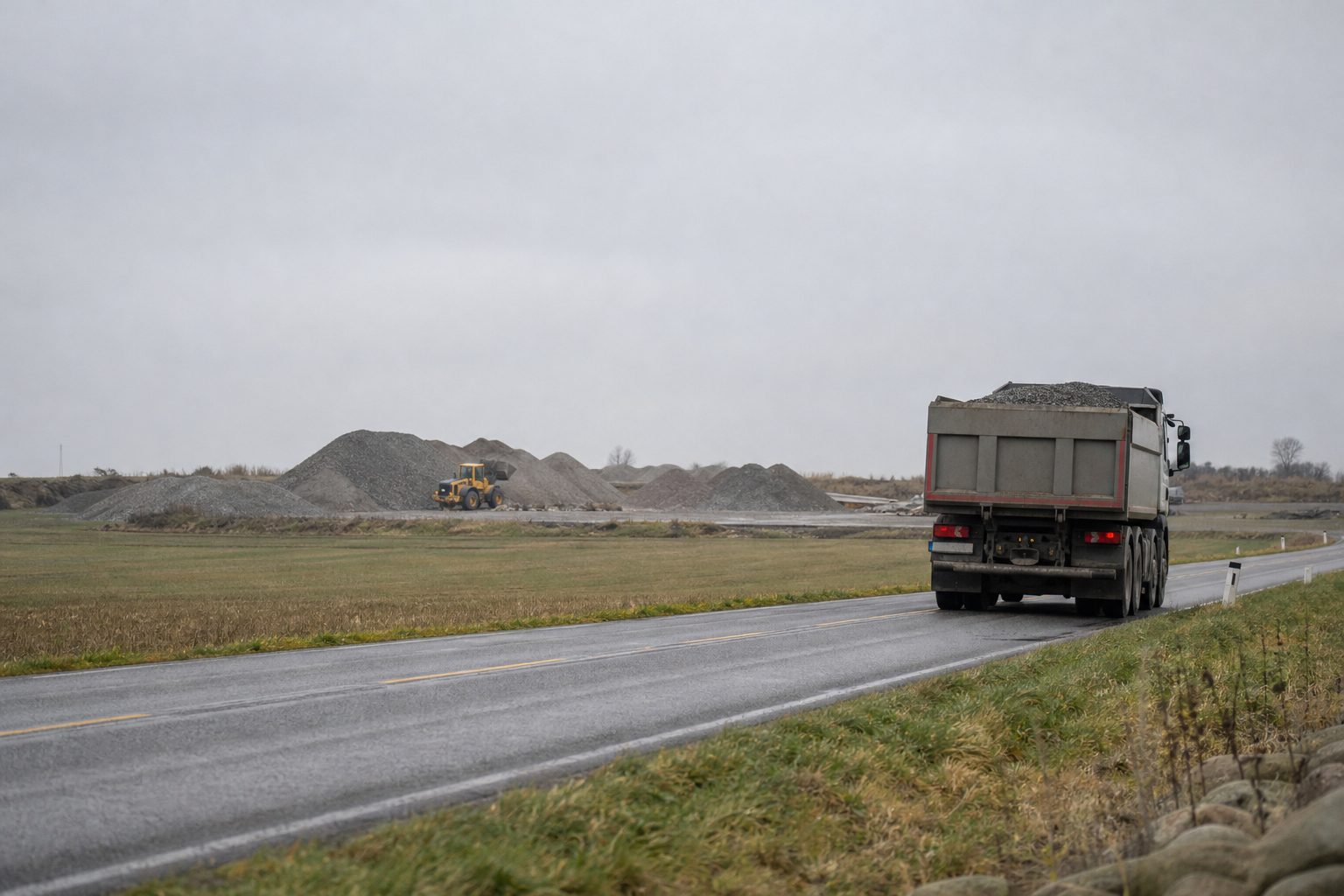En lastebil med grus kjører på en landevei mellom flate jorder på Jæren en grå høstdag.