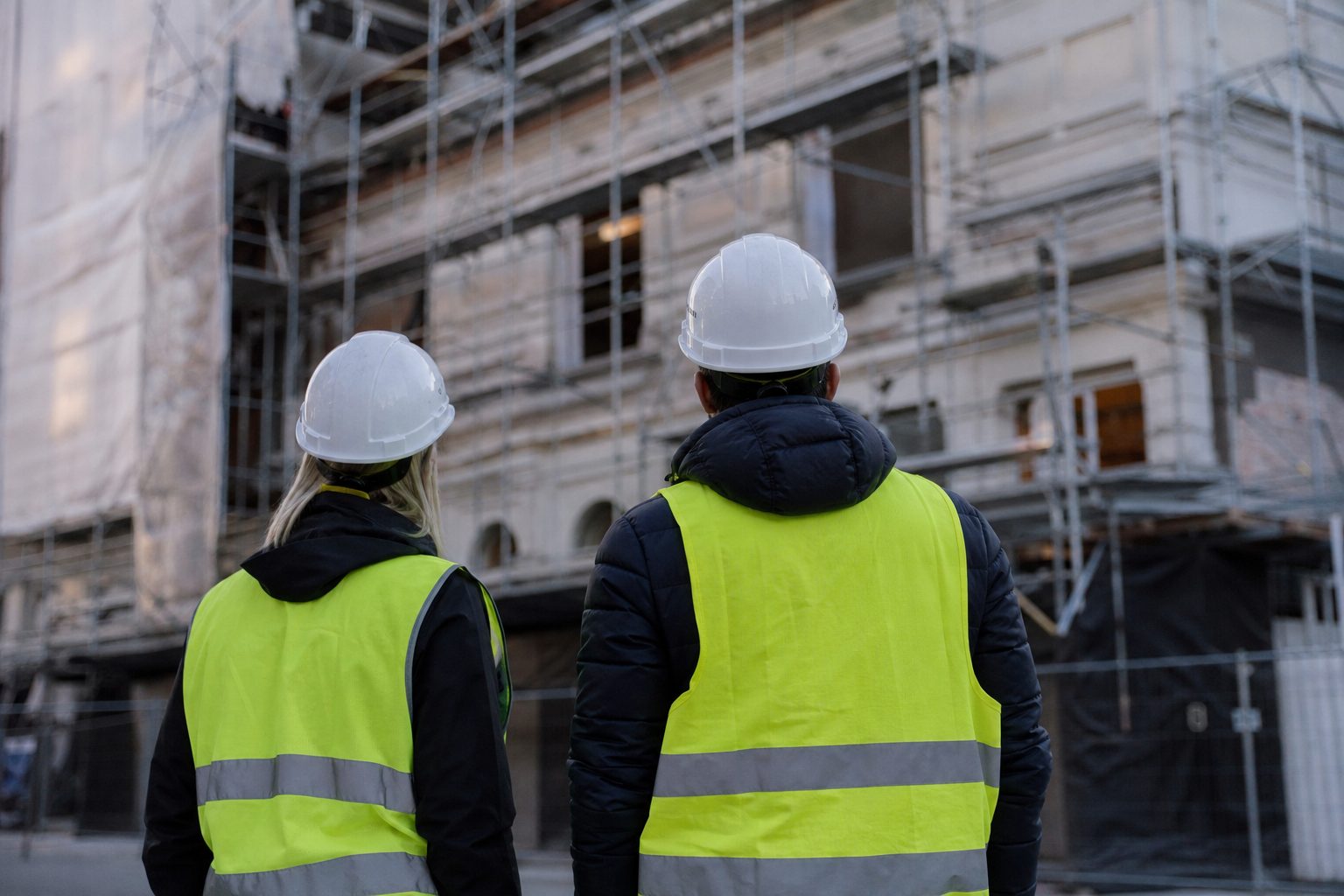 To personer med hjelm og refleksvest ser på et bygg under rehabilitering i Oslo.