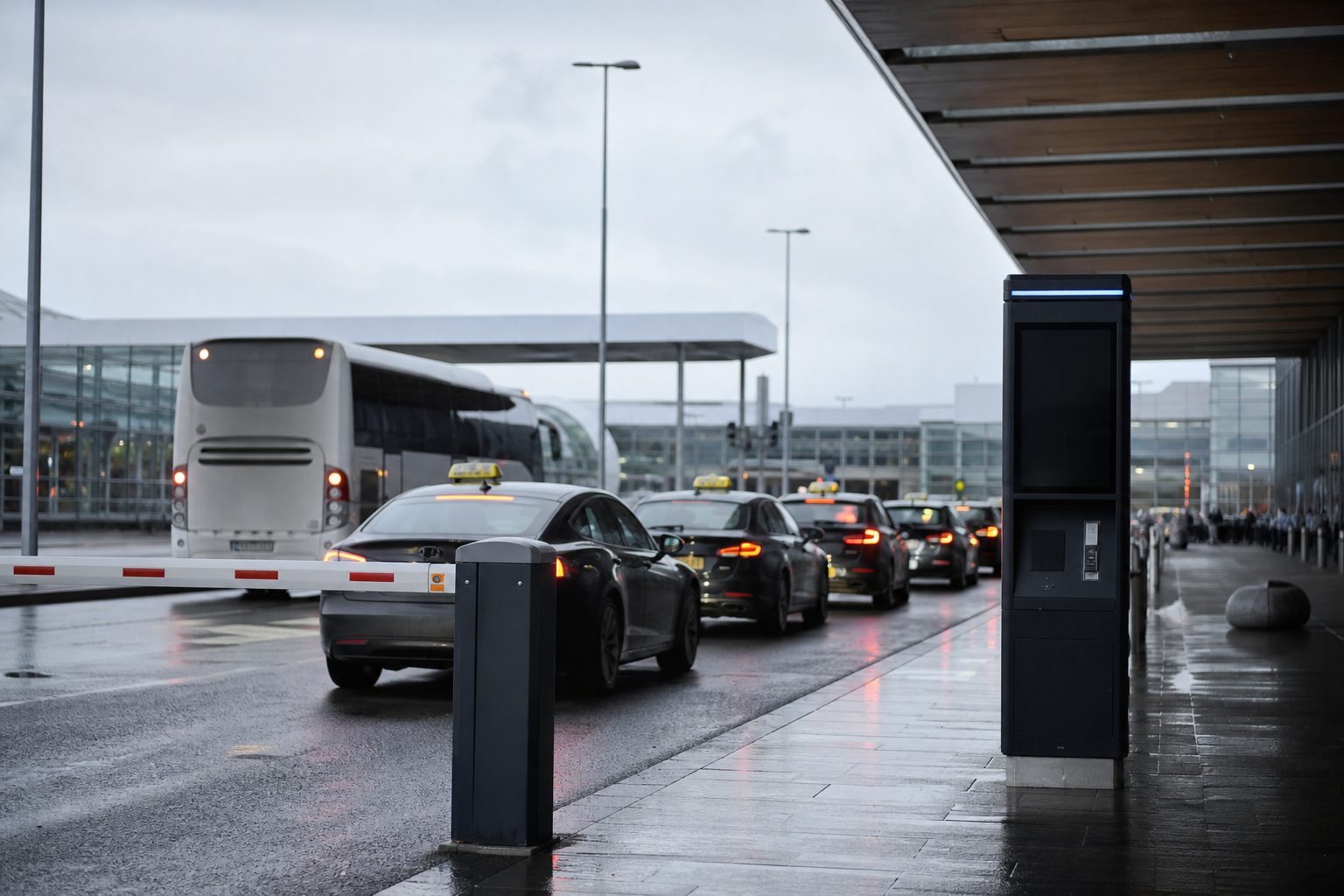 Forplassen utenfor en norsk lufthavnterminal en grå formiddag, med en rekke taxier ved en bom og en flybuss ved en plattform.