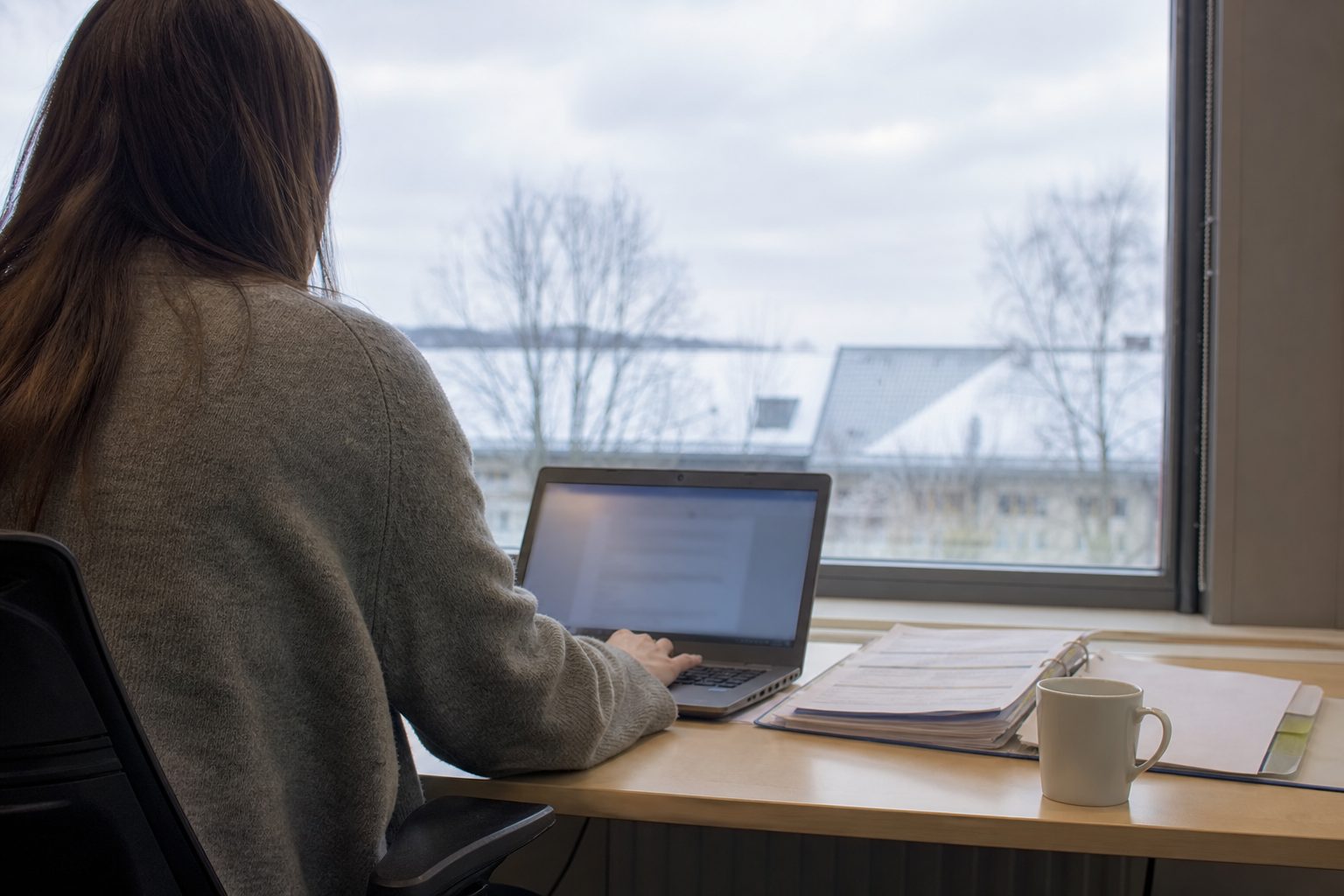 En innkjøper ved et skrivebord i et norsk kommunekontor skriver et kort notat på en bærbar PC.